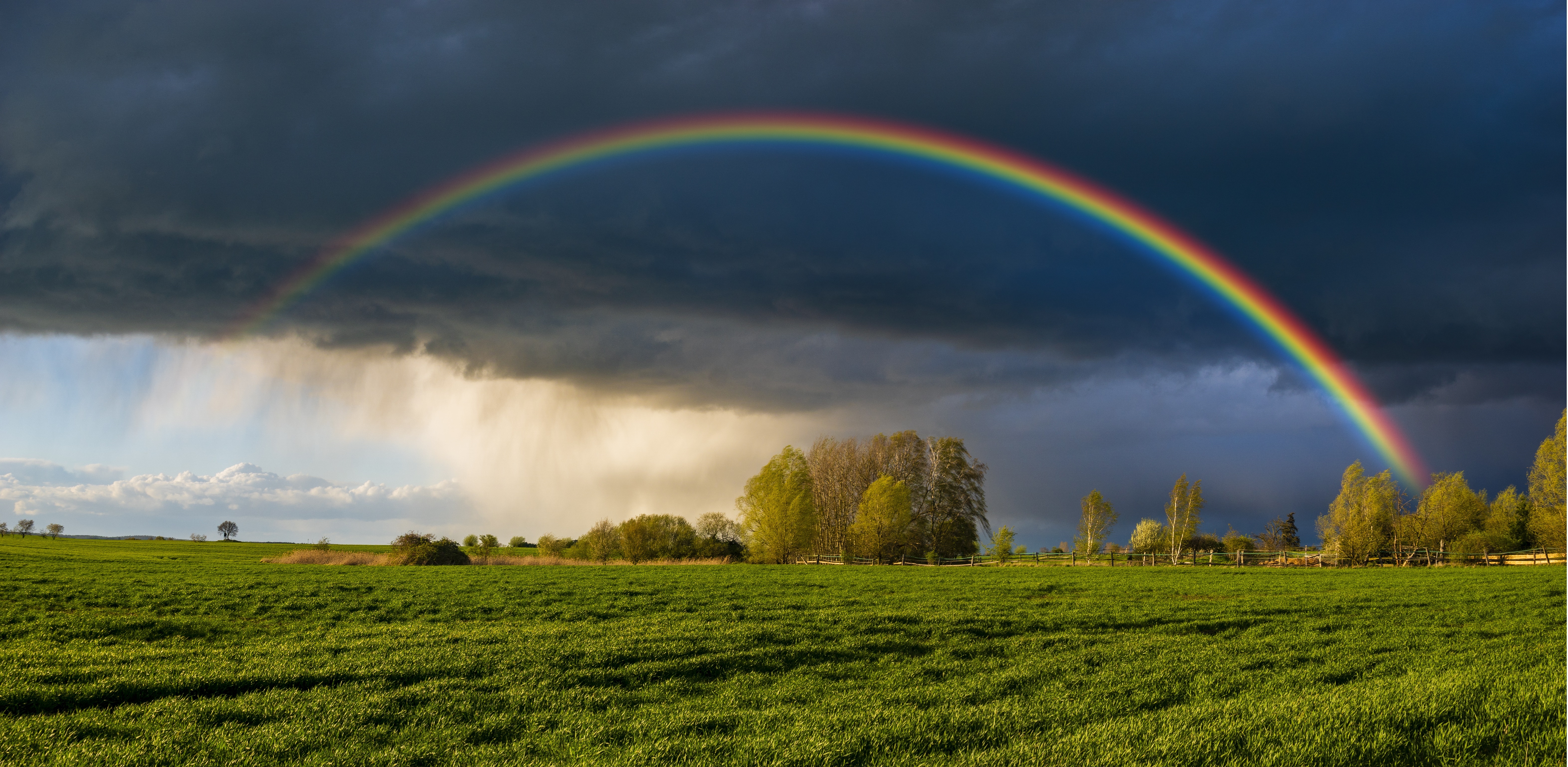a beautiful, colorful rainbow against the background of a dangerous, stormy sky over a rural farm